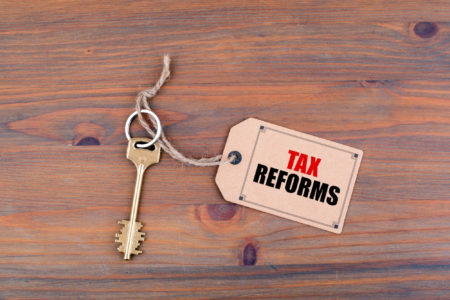 Key and a note on a wooden table with text - Tax Reforms